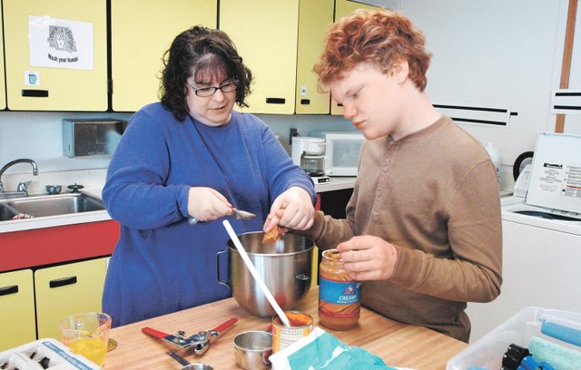 With+the+help+of+teacher+Judith+White%2C+left%2C+eighth-grader+Reed+Hosley+scoops+peanut+butter+into+a+mixing+bowl.%0A