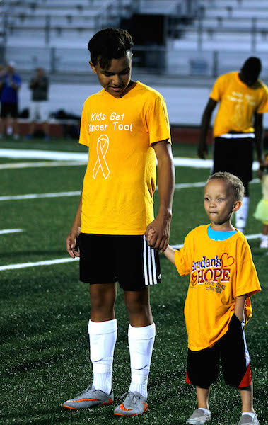 Oscar Aguliar Jr. holds hands with a kid that has survived cancer