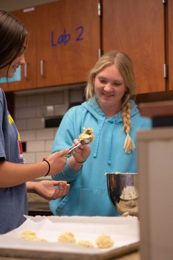 Helping scoop the cookies, Sophomore Madison Bruson helps her classmate  Sophomore, Eve Frame  scoop cookies. Bruson said, “I was trying to get every piece of the cookies off the pan to place.
